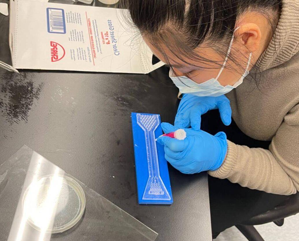 Student in lab coat smiles and holds of vial of liquid metal